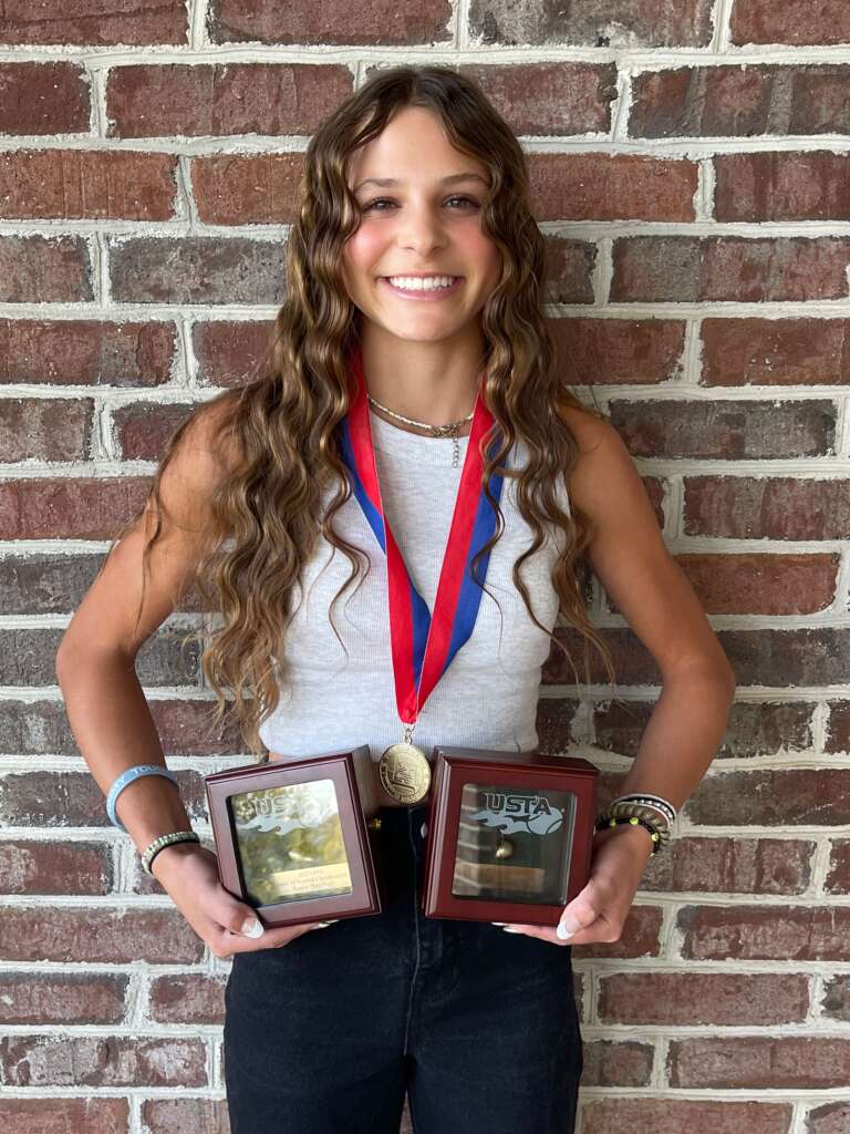 Anna Frey holding a few of her awards after a tournament while smiling for the camera. 